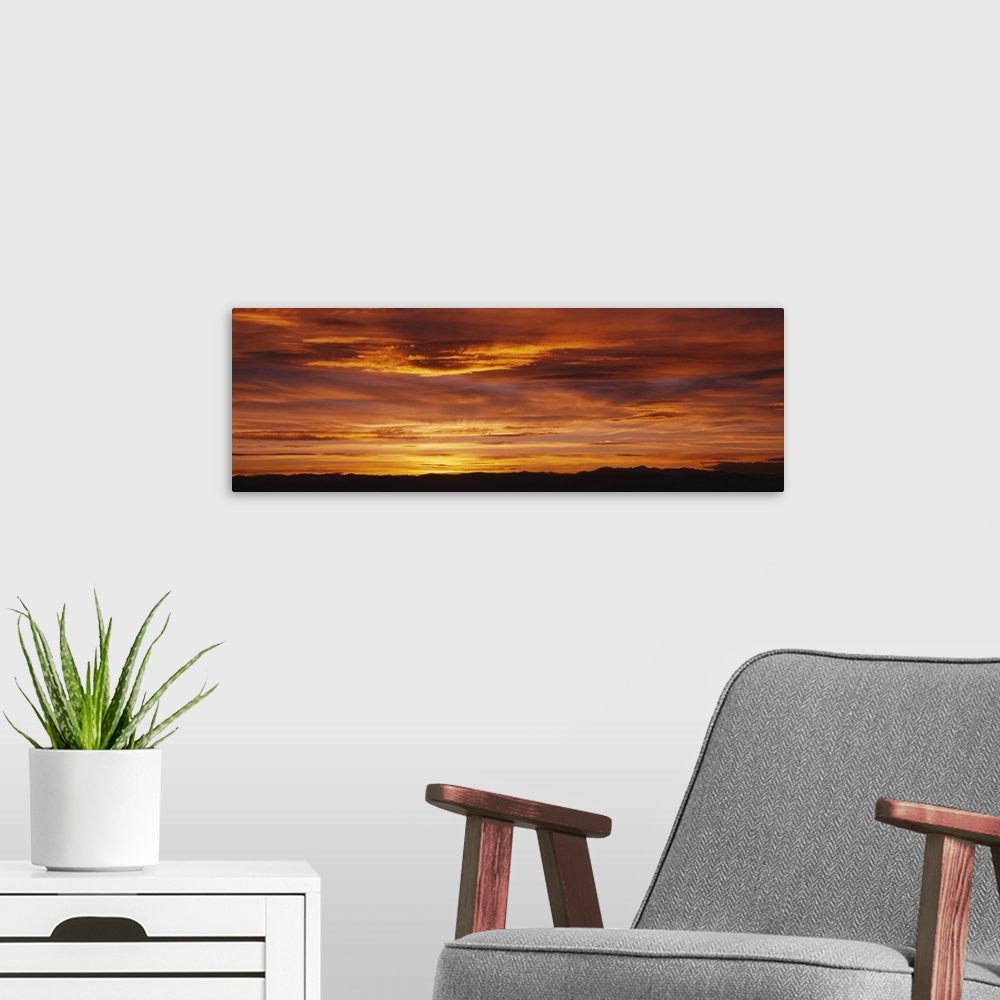 A modern room featuring Long panoramic image of the sun setting on the horizon creating a brilliant color show of fire-li...