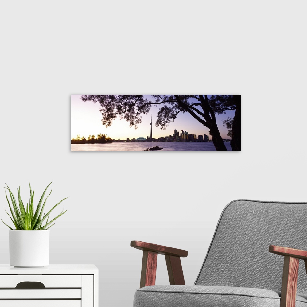 A modern room featuring Landscape photograph on a giant canvas of a large tree hanging over the water as the sun sets, th...