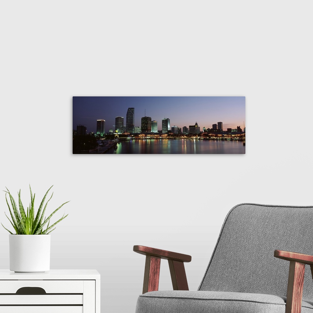 A modern room featuring Long print of a cityscape along the water in Florida lit up at dusk.