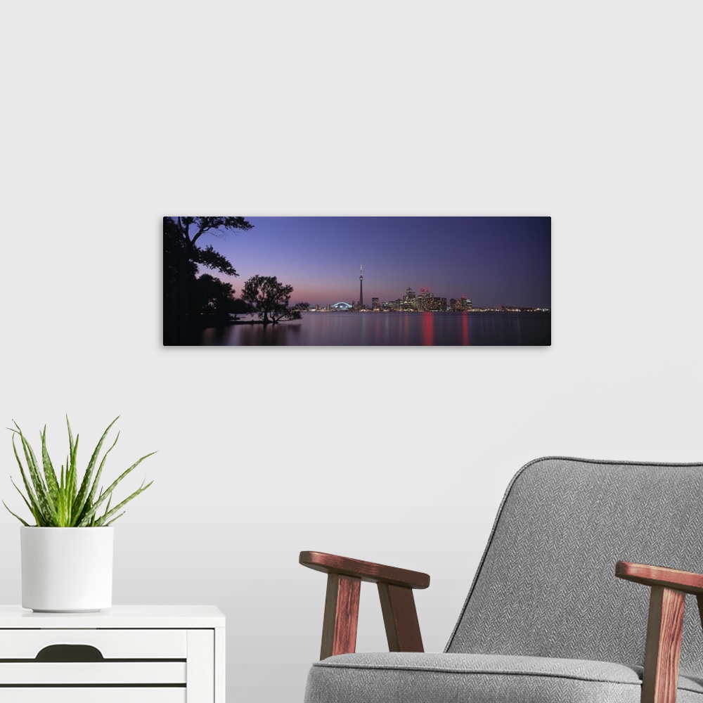 A modern room featuring A panoramic photograph taken at twilight of the city skyline in the distance reflecting in the wa...