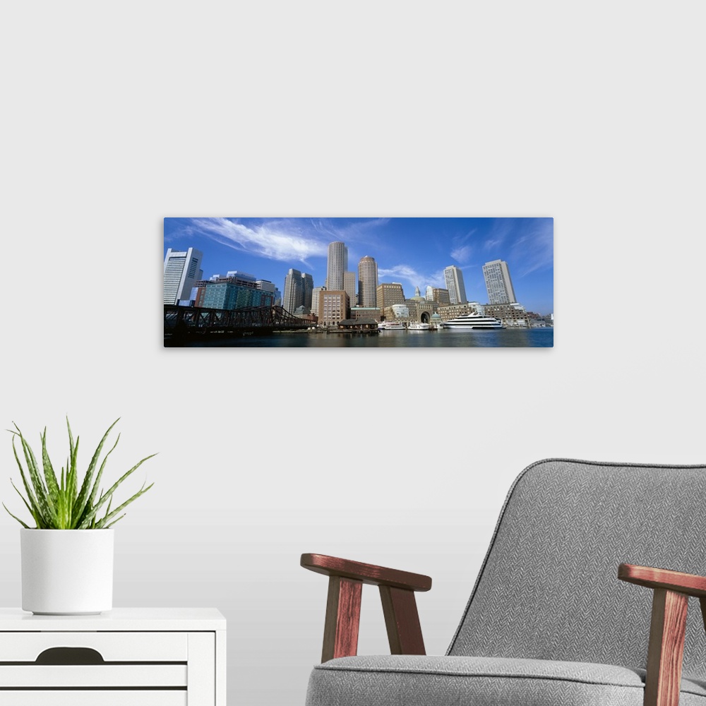 A modern room featuring The Boston skyline is photographed in panoramic view from the waterfront during a bright sunny day.