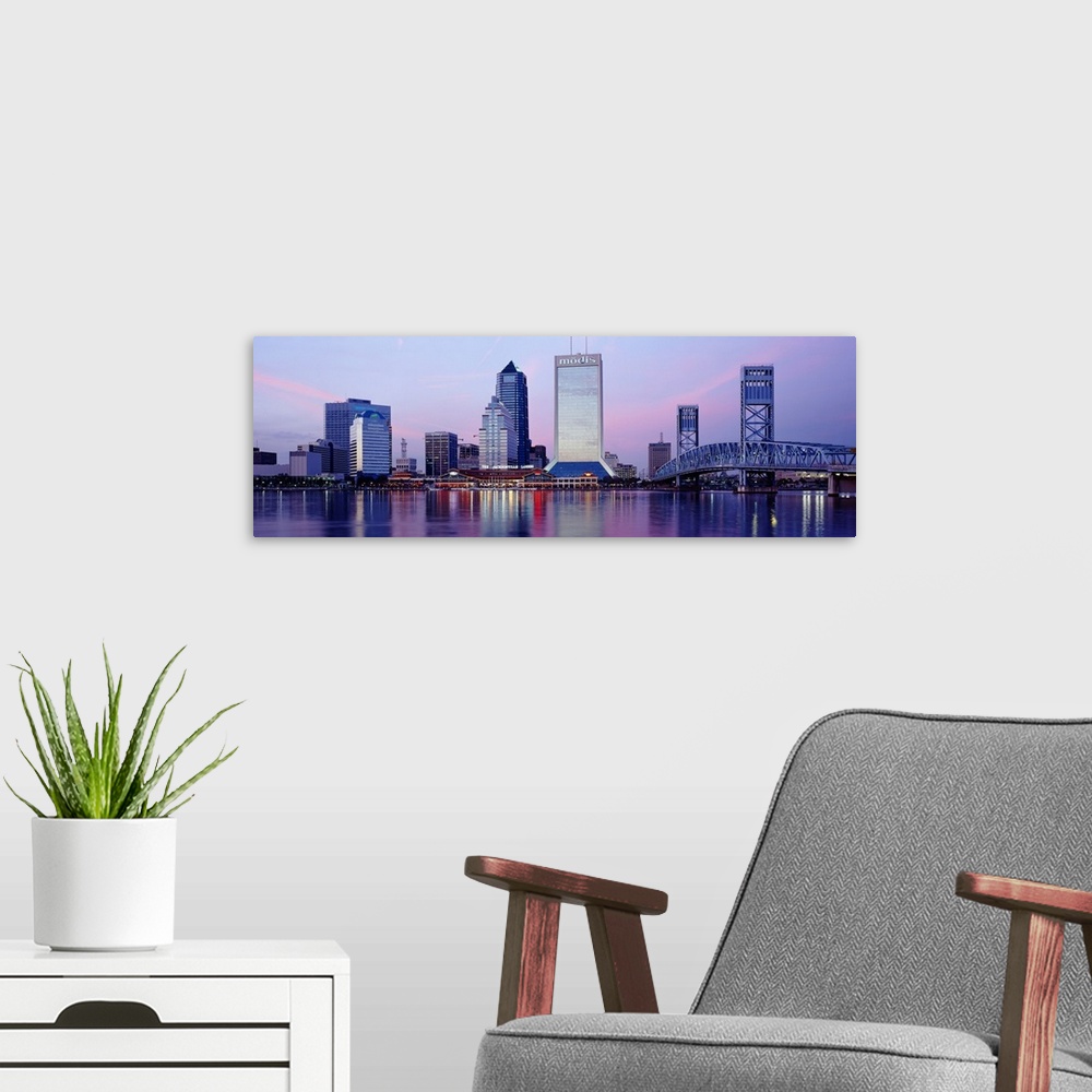 A modern room featuring A panorama view of the city skyline in Jacksonville during dusk. The buildings lights reflect in ...