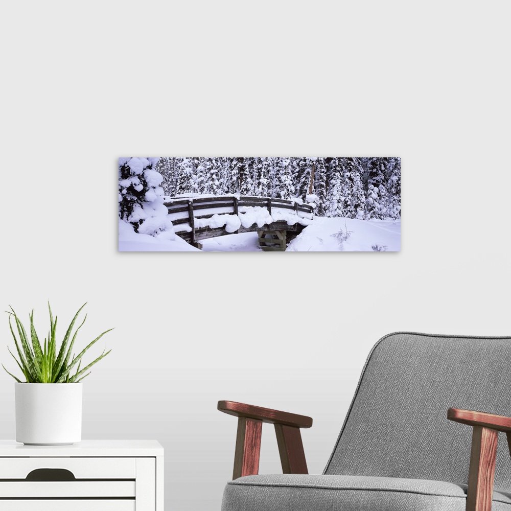 A modern room featuring Long horizontal photo on canvas of a heavily snow covered bridge in the middle of a forest.