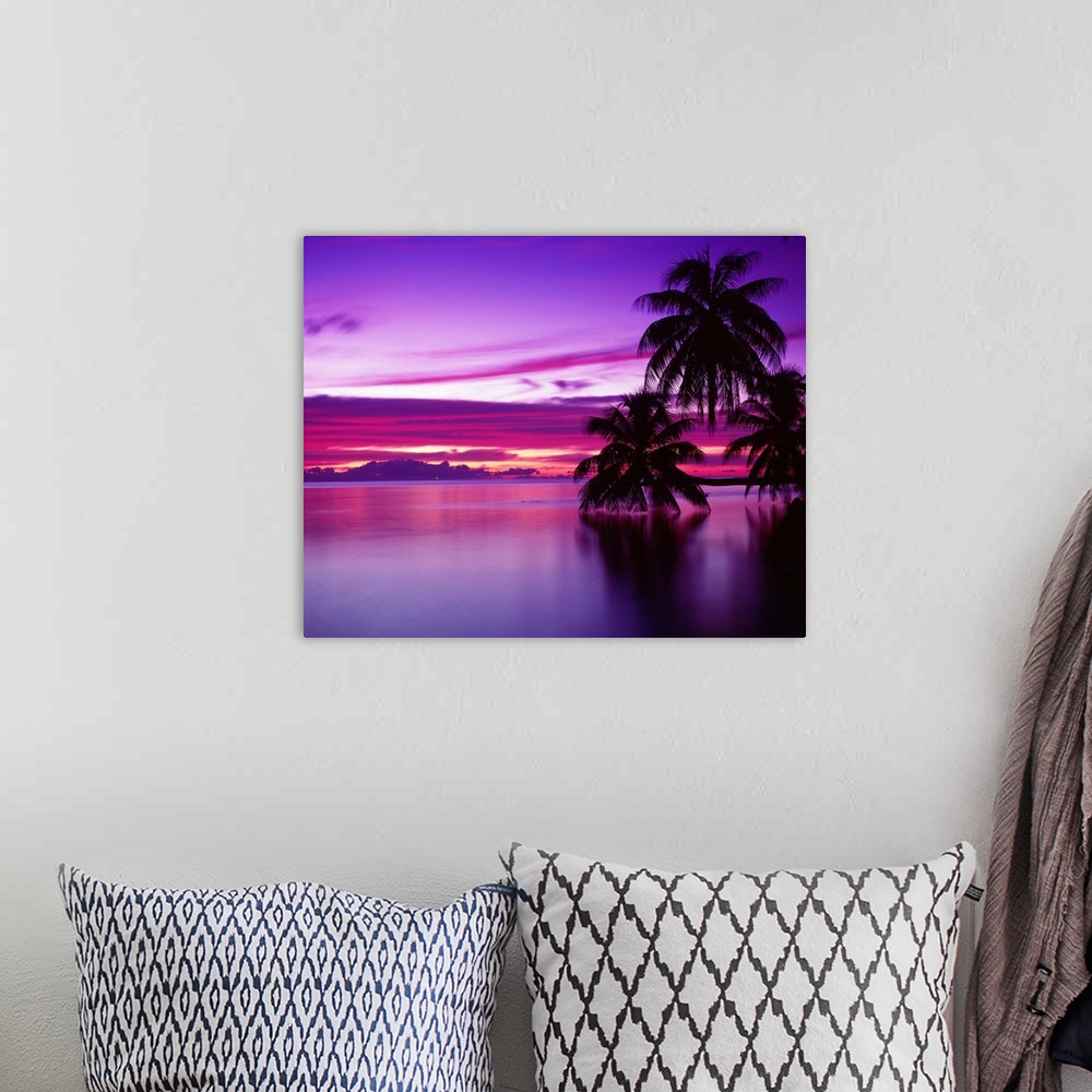 A bohemian room featuring Canvas photo art of a peaceful ocean with big palm trees silhouetted against a bright sunset.