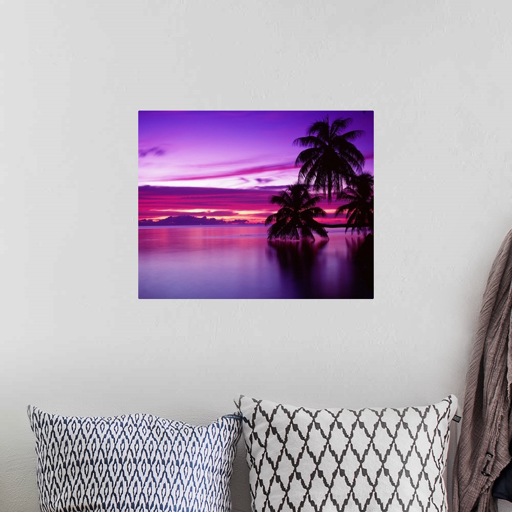 A bohemian room featuring Canvas photo art of a peaceful ocean with big palm trees silhouetted against a bright sunset.