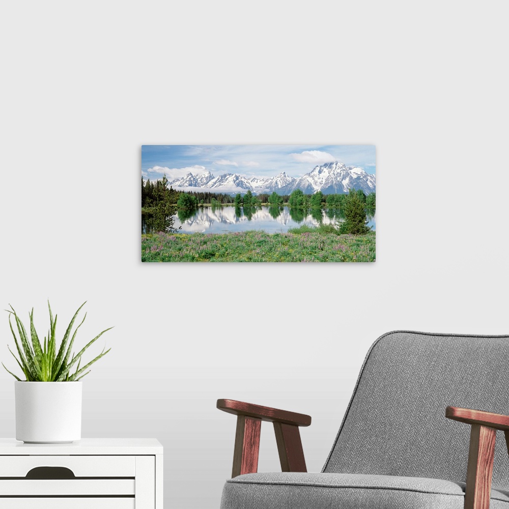 A modern room featuring Large photo on canvas of a rugged mountain range with a lake in the foreground and a tree line se...