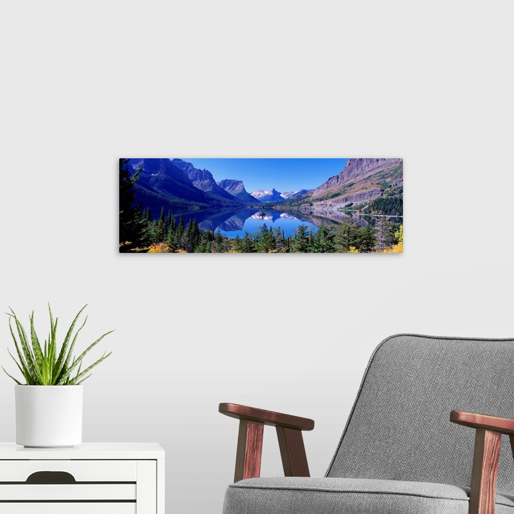 A modern room featuring A photographic print of rugged mountains with snow in the distance reflected in a crystal clear l...