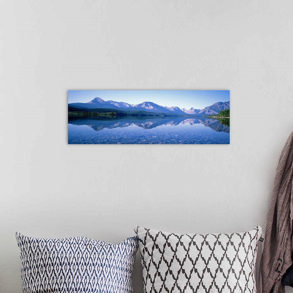A bohemian room featuring Mountains line the back of this panoramic photograph that is taken from across a crystal clear la...