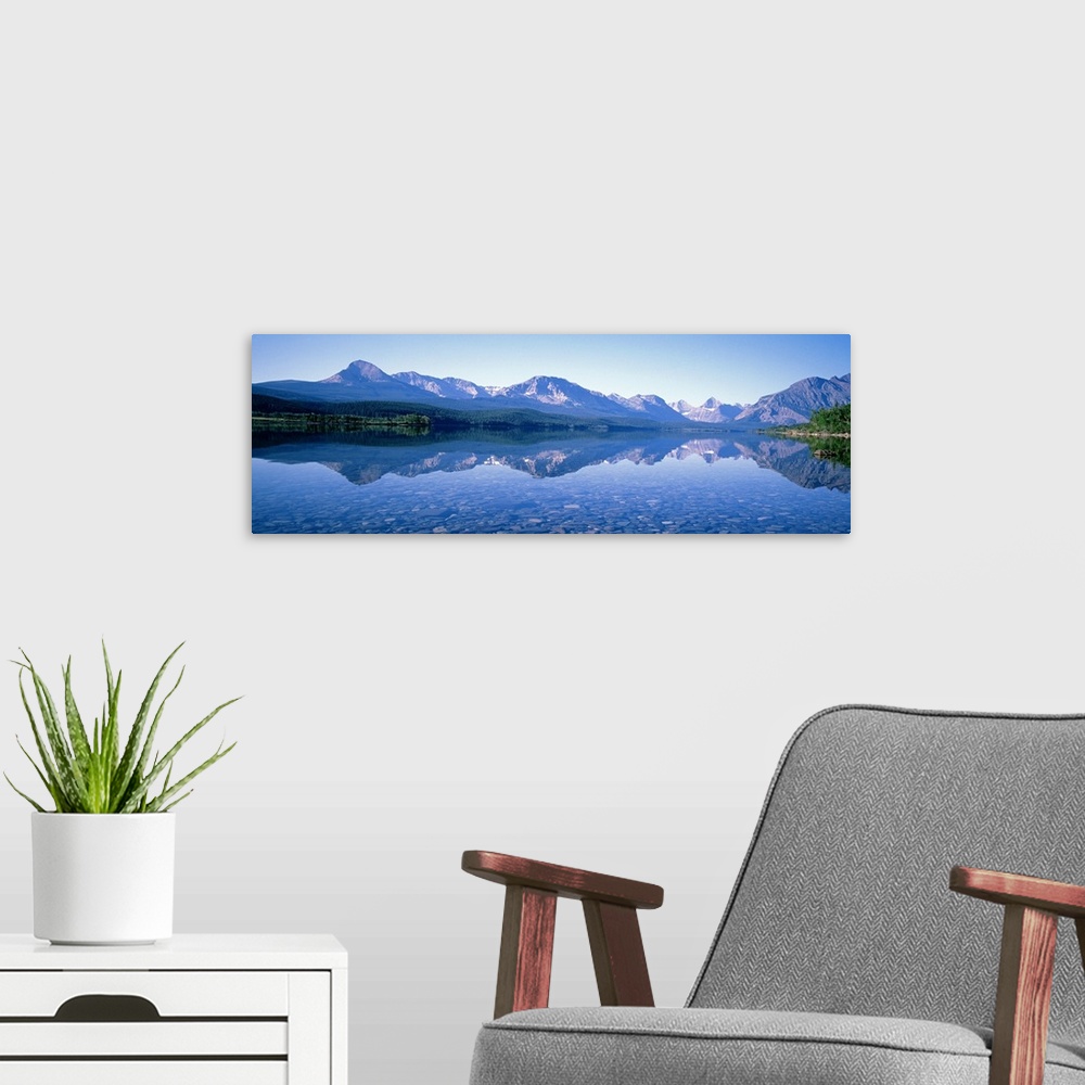 A modern room featuring Mountains line the back of this panoramic photograph that is taken from across a crystal clear la...