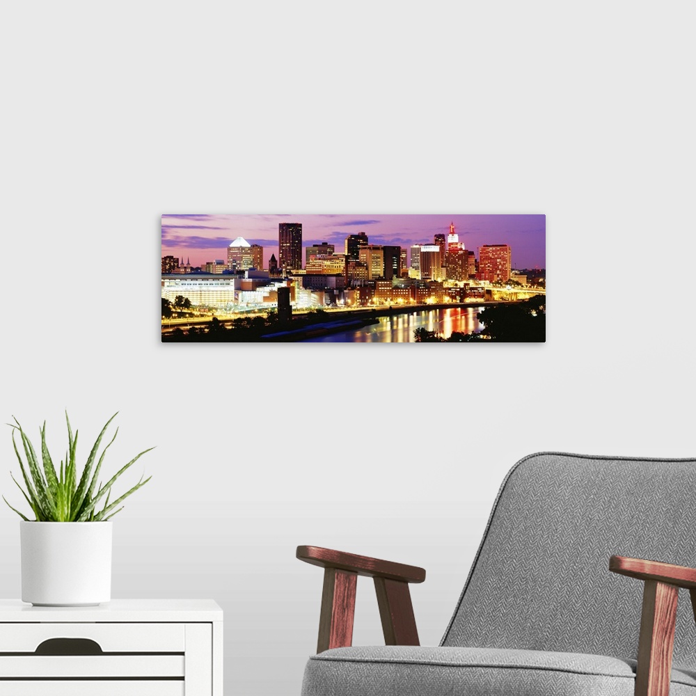 A modern room featuring Panoramic photograph of city skyline on a cloudy night.  The building lights are glowing and they...
