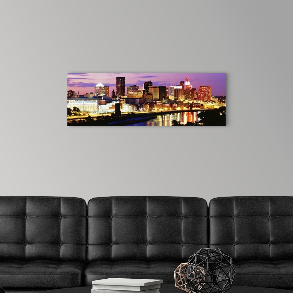 A modern room featuring Panoramic photograph of city skyline on a cloudy night.  The building lights are glowing and they...