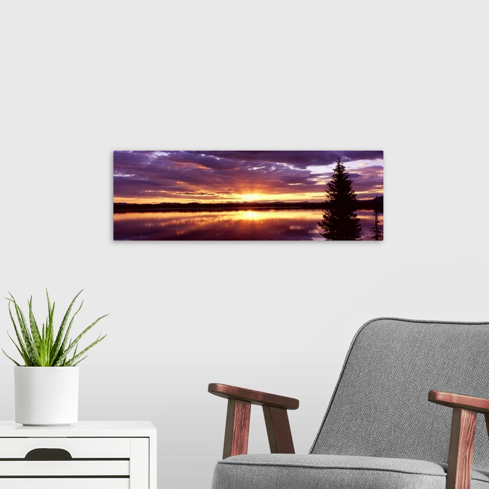 A modern room featuring Long horizontal canvas of the sun rising through stormy clouds reflected onto the lake.