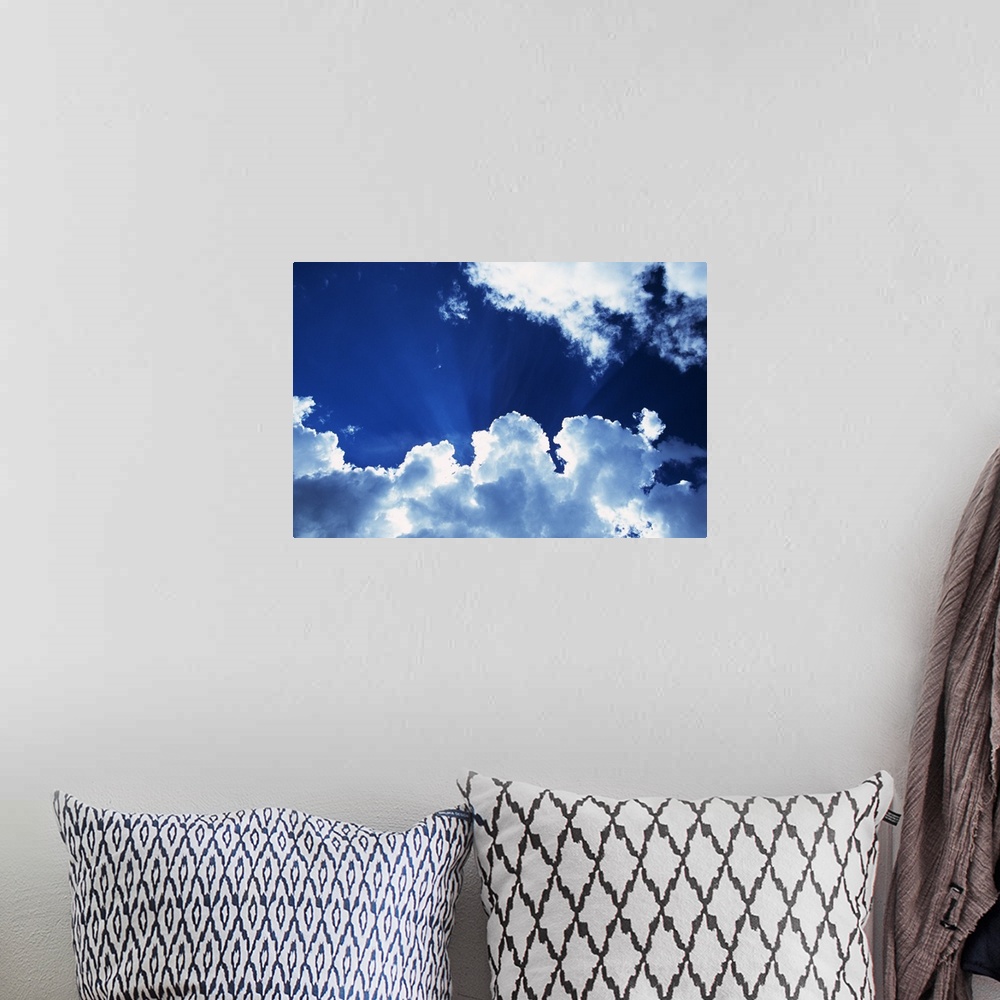 A bohemian room featuring Sunbeams behind billowing white clouds, blue sky.