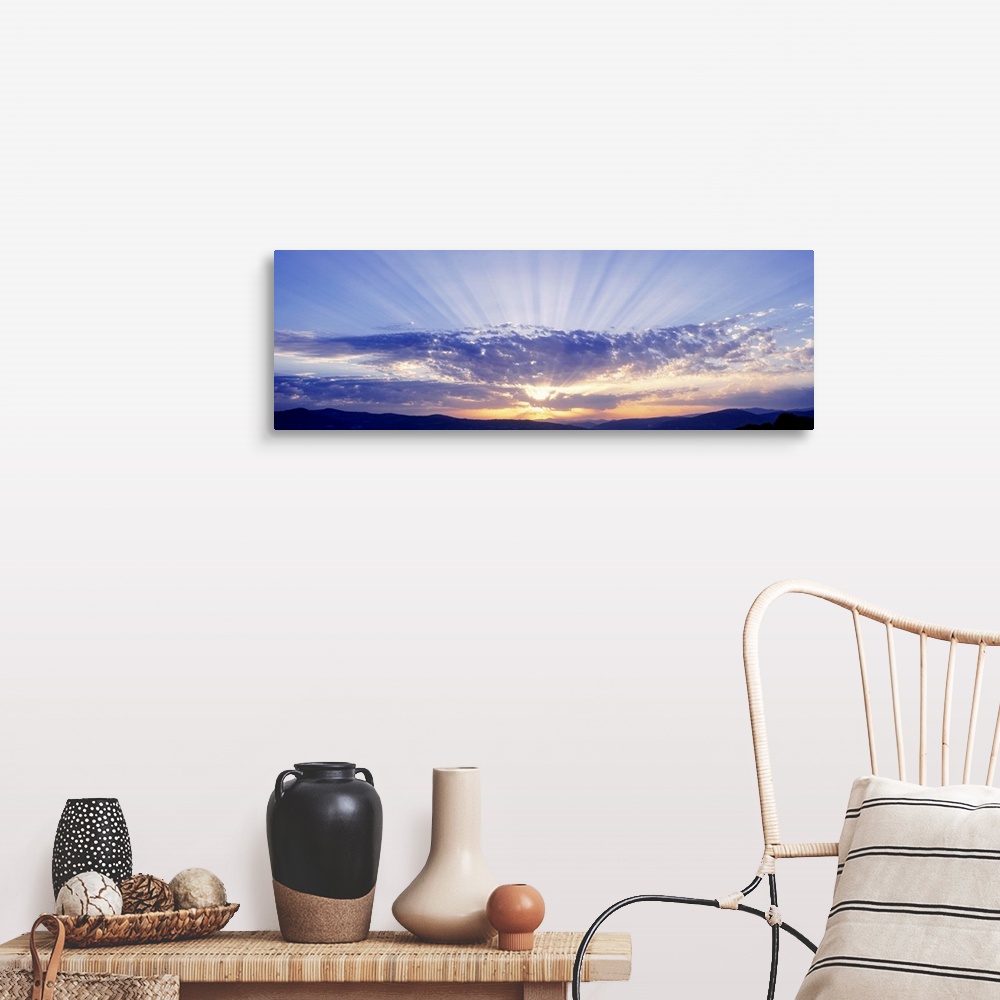 A farmhouse room featuring This panoramic wall art captures as a photograph radiant sun beams radiate from behind clouds ove...