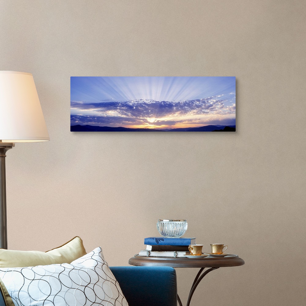 A traditional room featuring This panoramic wall art captures as a photograph radiant sun beams radiate from behind clouds ove...