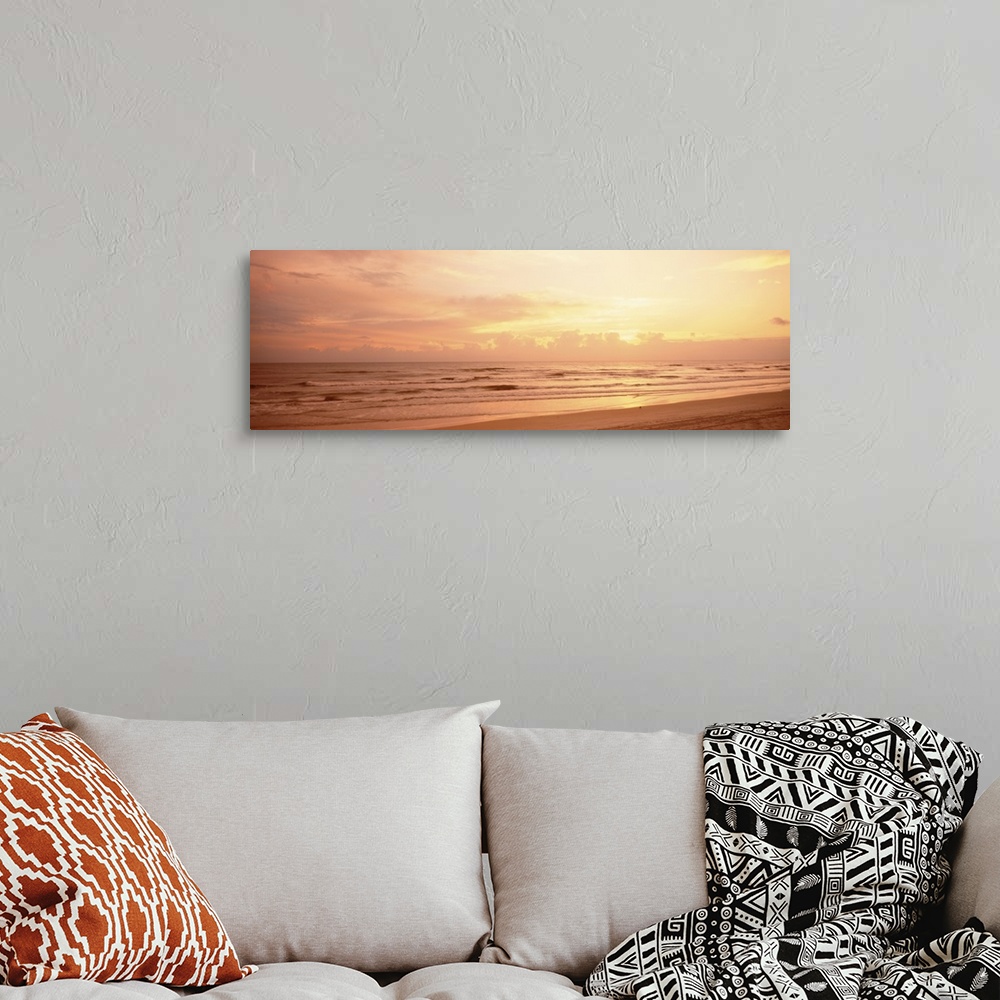 A bohemian room featuring Panoramic photograph of the sun rising above the clouds as small waves break on the sandy shore.