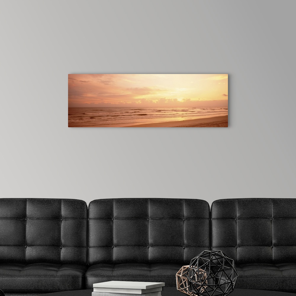 A modern room featuring Panoramic photograph of the sun rising above the clouds as small waves break on the sandy shore.