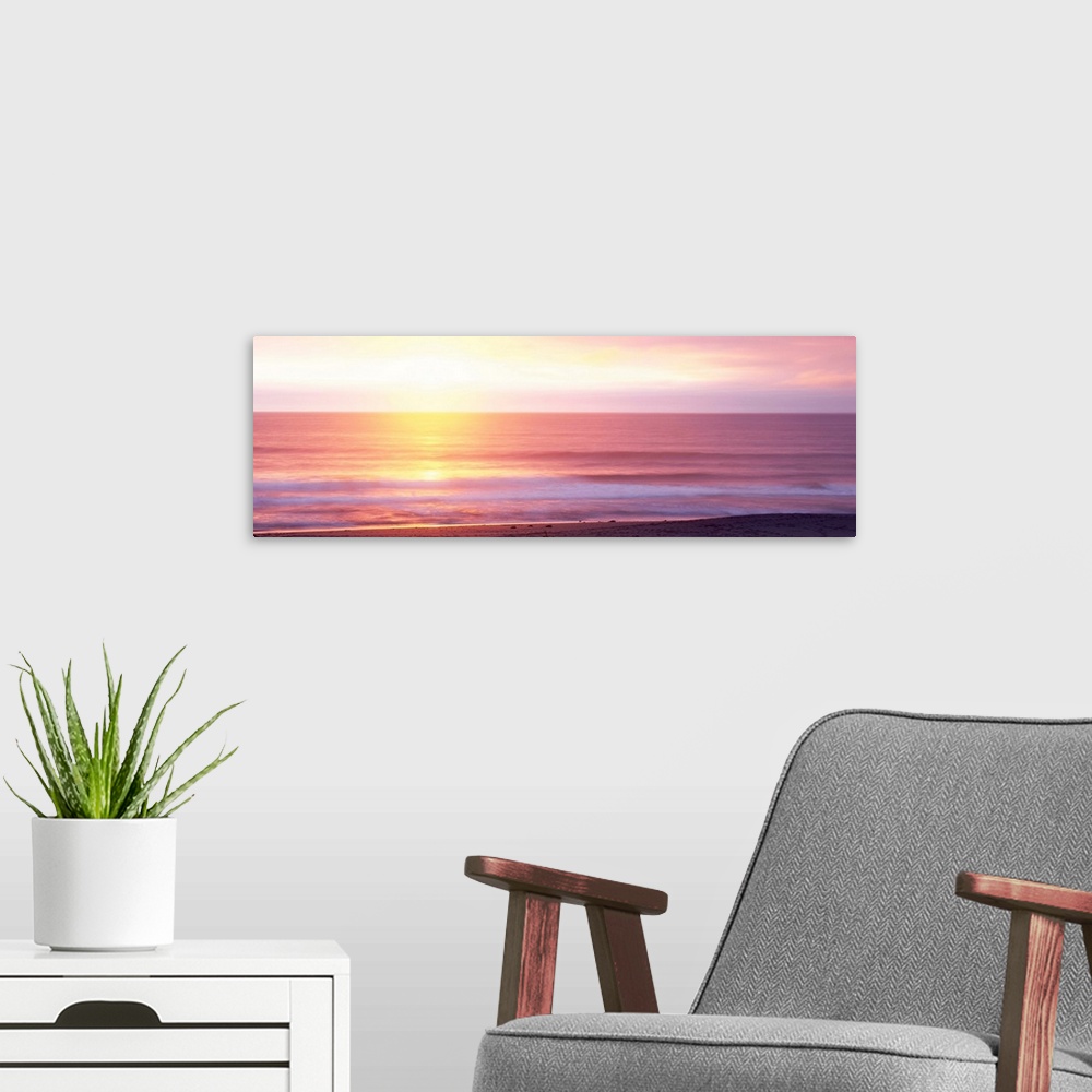 A modern room featuring A panoramic photograph taken of the sunrise over a vast ocean off a coast in Hawaii.