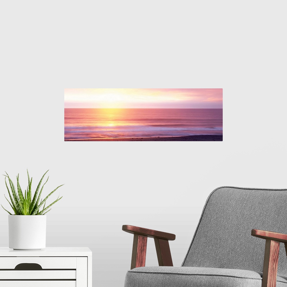 A modern room featuring A panoramic photograph taken of the sunrise over a vast ocean off a coast in Hawaii.
