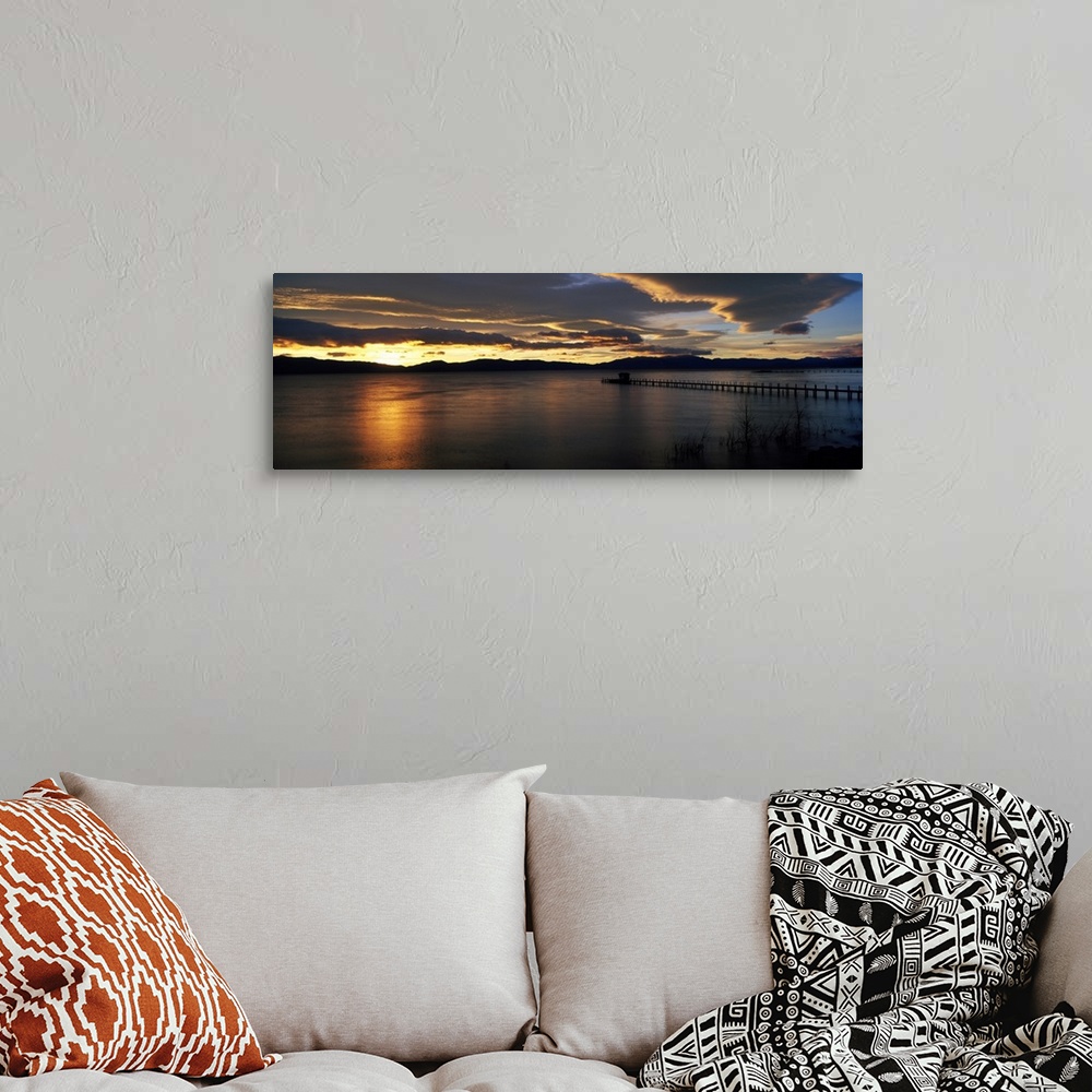 A bohemian room featuring Panoramic photograph of pier stretching into water at dawn.  The sky is dark and cloudy.