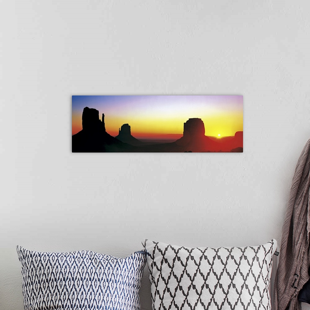 A bohemian room featuring The sun begins to rise and silhouette Monument Valley in a wide angle view.