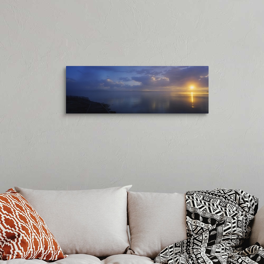A bohemian room featuring Panoramic photograph of walkway alongside ocean at dawn under a cloudy sky.