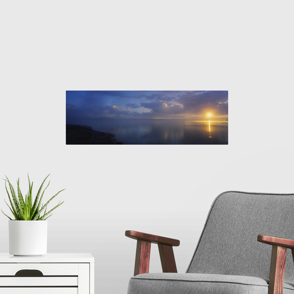 A modern room featuring Panoramic photograph of walkway alongside ocean at dawn under a cloudy sky.