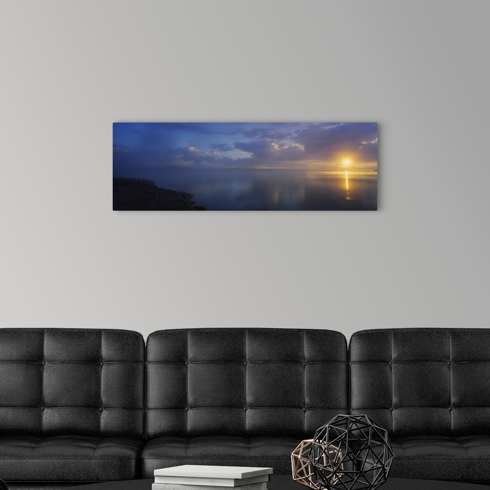 A modern room featuring Panoramic photograph of walkway alongside ocean at dawn under a cloudy sky.