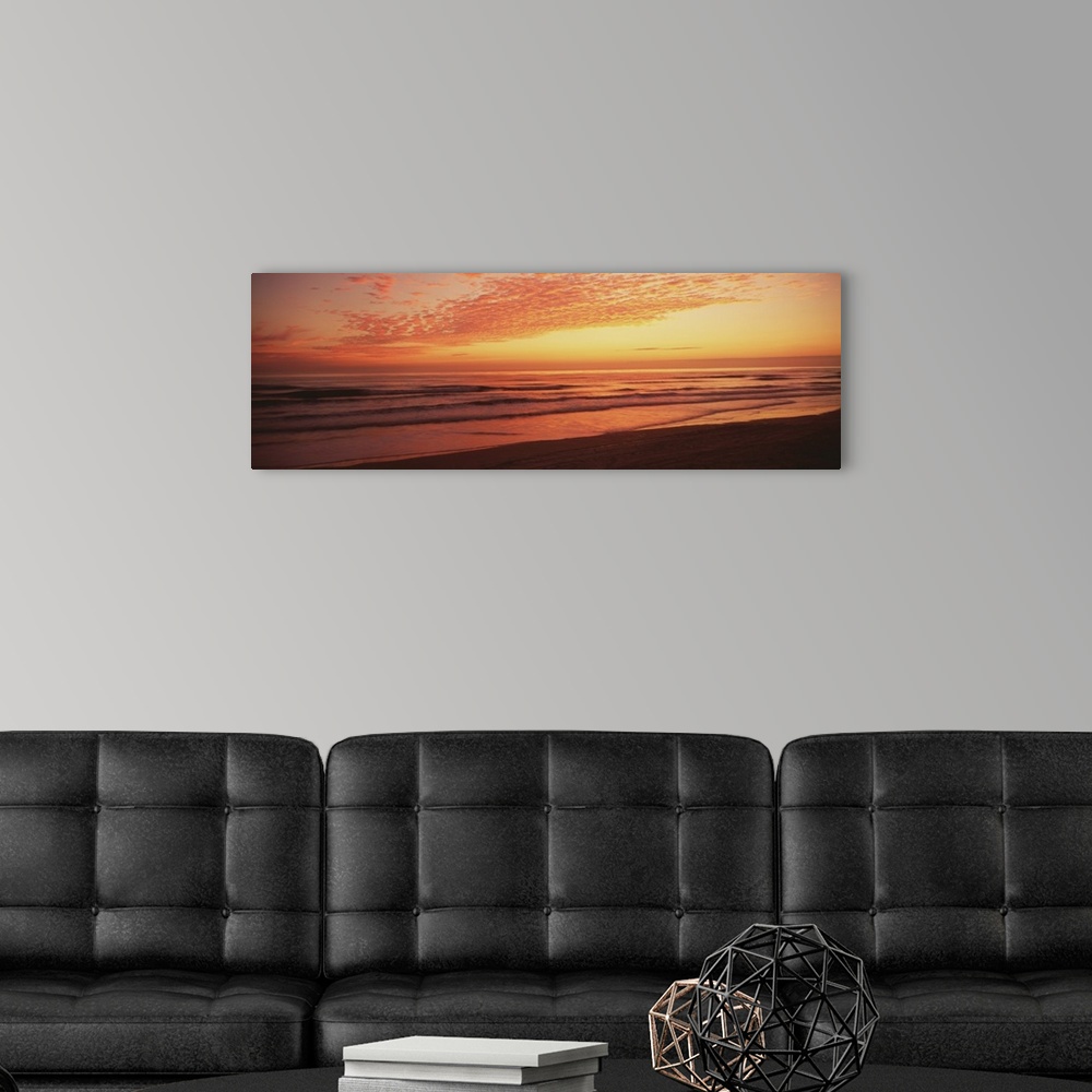 A modern room featuring Large, wide angle photograph of a golden sunrise over the Atlantic Ocean, at the shoreline of Day...