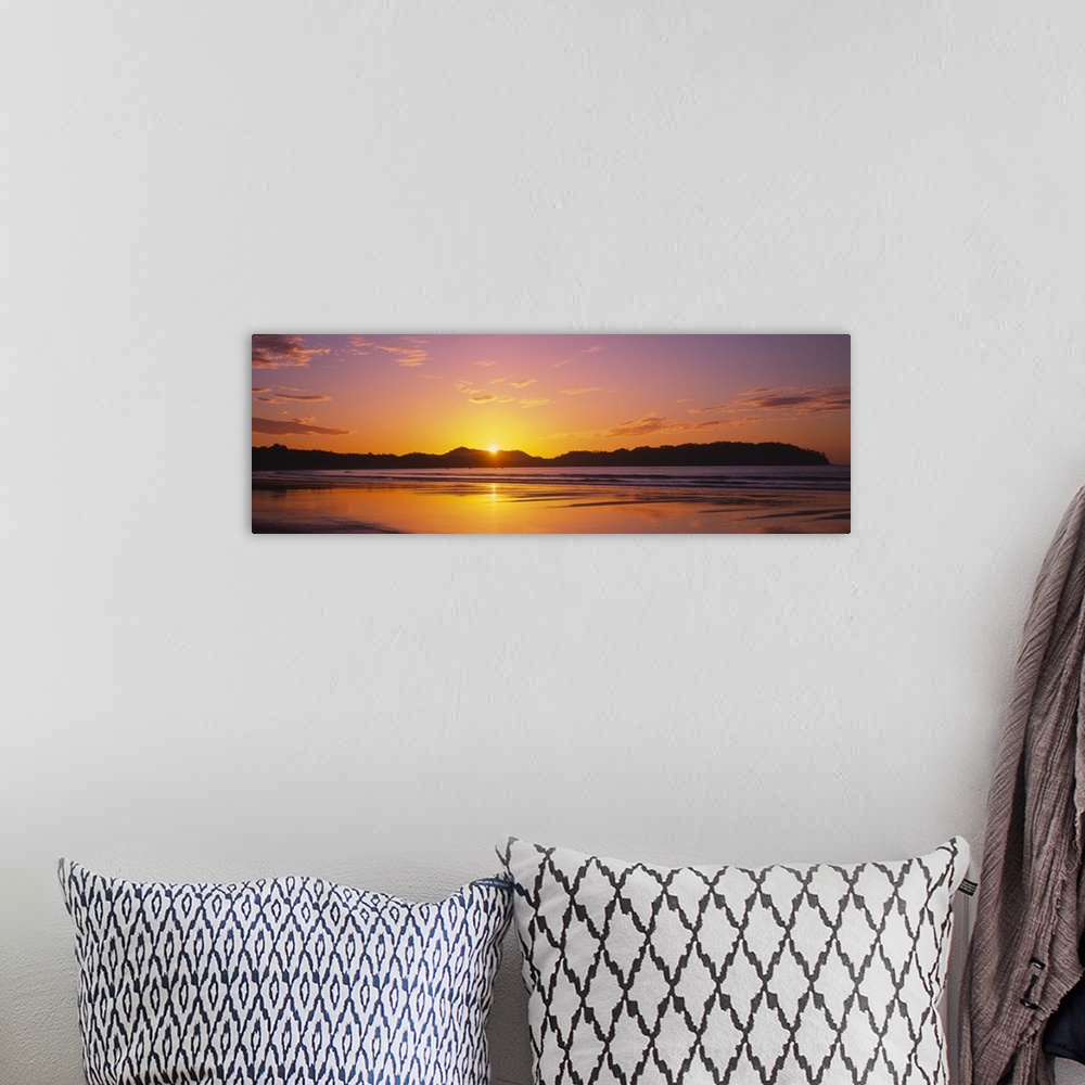 A bohemian room featuring Long and horizontal image of the sun rising above a mountain near a beach in Costa Rica.