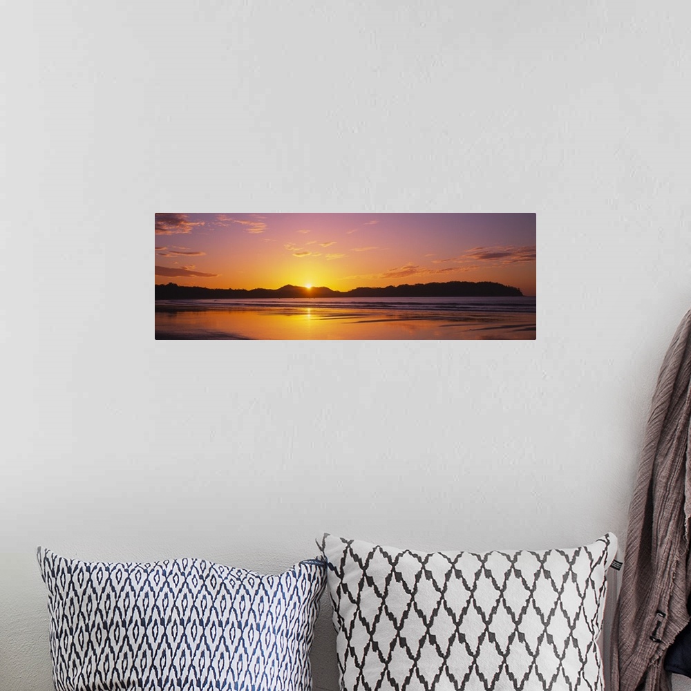 A bohemian room featuring Long and horizontal image of the sun rising above a mountain near a beach in Costa Rica.