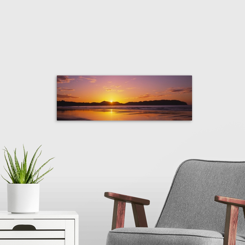 A modern room featuring Long and horizontal image of the sun rising above a mountain near a beach in Costa Rica.