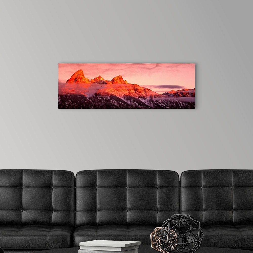 A modern room featuring The sun rises on rugged mountains casting a warm hue of sunlight over the tops of them with darkn...