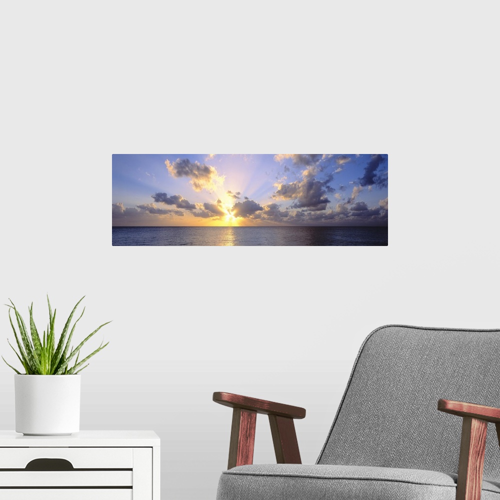 A modern room featuring Giant panoramic photograph of the sun about to set in the distance from the perspective of a beac...