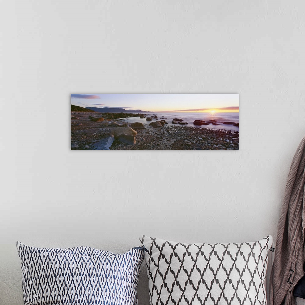 A bohemian room featuring Panoramic photograph of rock and pebble filled shoreline with sun setting in the distance.