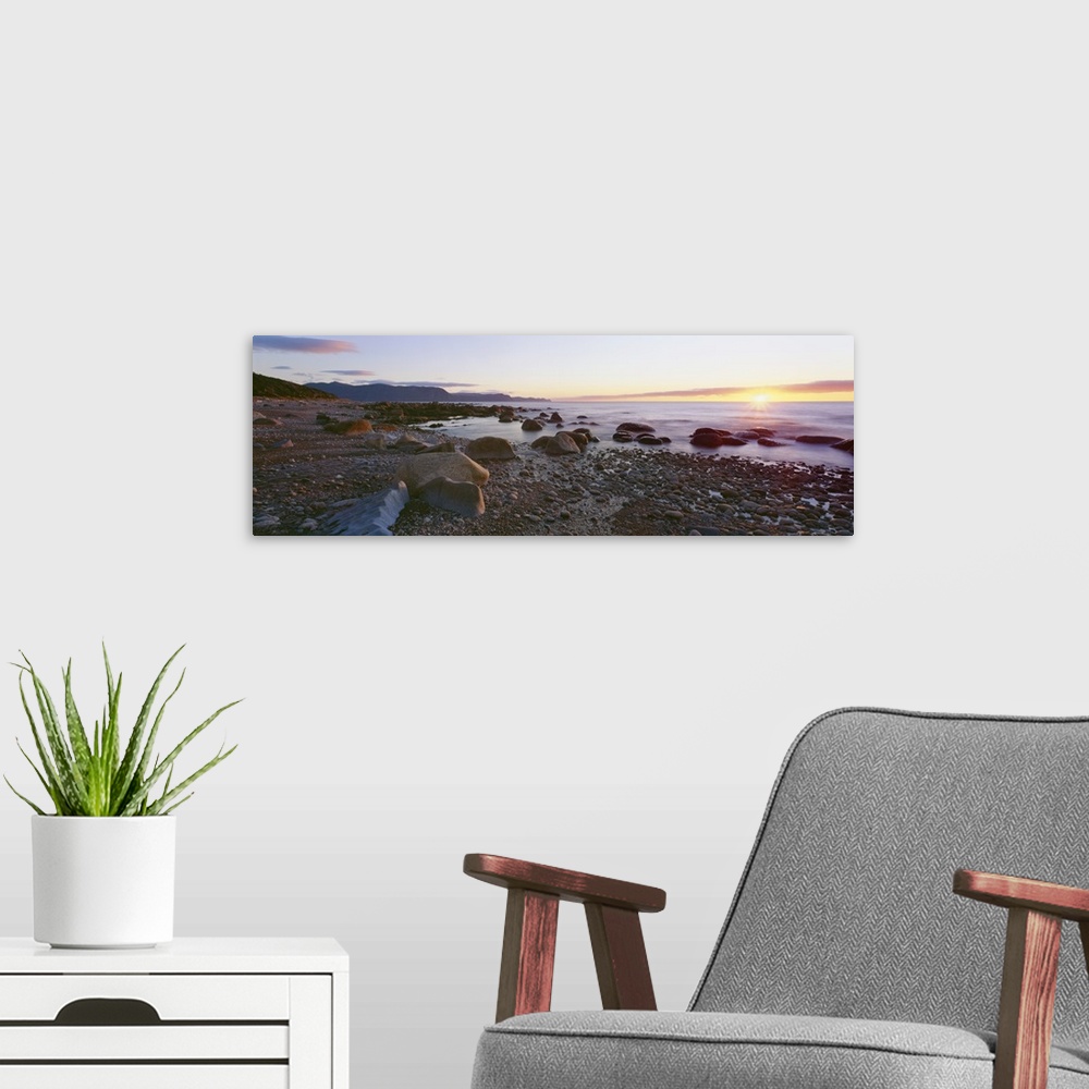 A modern room featuring Panoramic photograph of rock and pebble filled shoreline with sun setting in the distance.