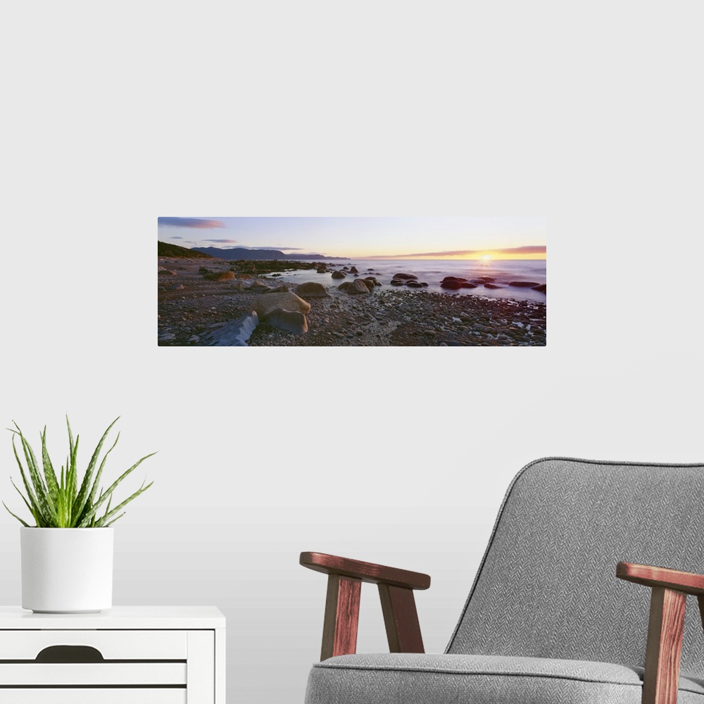 A modern room featuring Panoramic photograph of rock and pebble filled shoreline with sun setting in the distance.