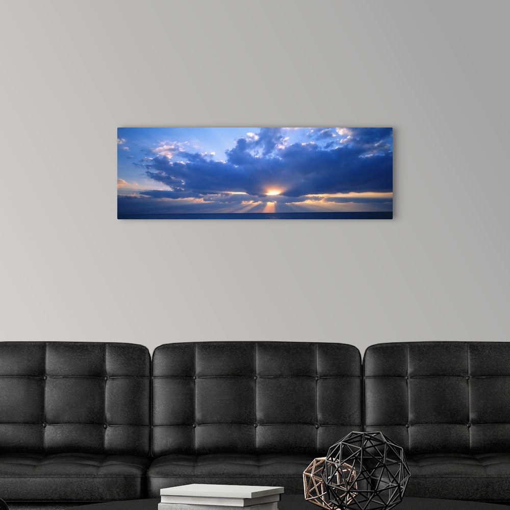 A modern room featuring Panoramic photograph of the sun peaking through large, fluffy clouds as it sets over the Gulf of ...