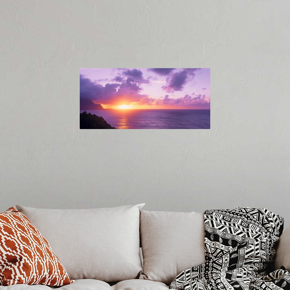A bohemian room featuring Sun setting on the ocean horizon creating a pastel-colored sky in the evening in Hawaii. Large la...