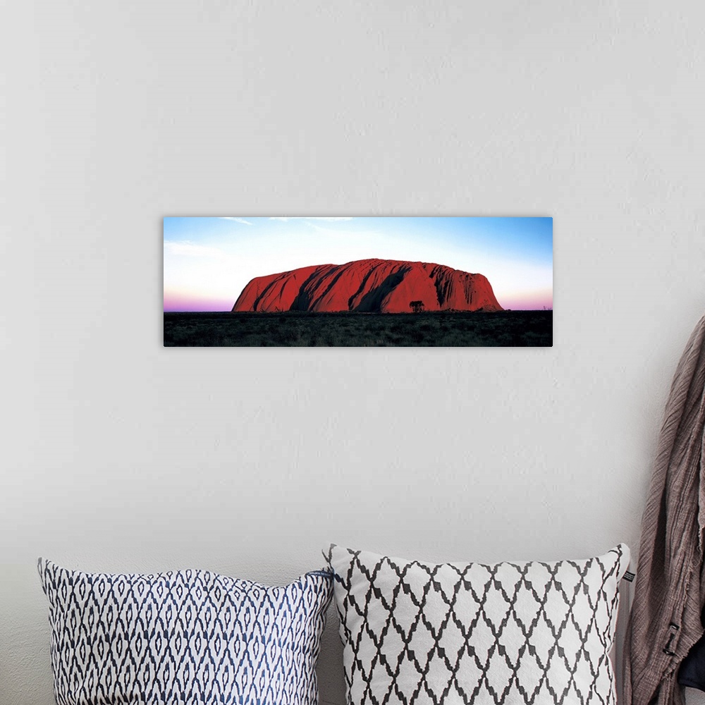 A bohemian room featuring The Ayers Rock is photographed in wide angle view during a sunset which lines the horizon with wa...