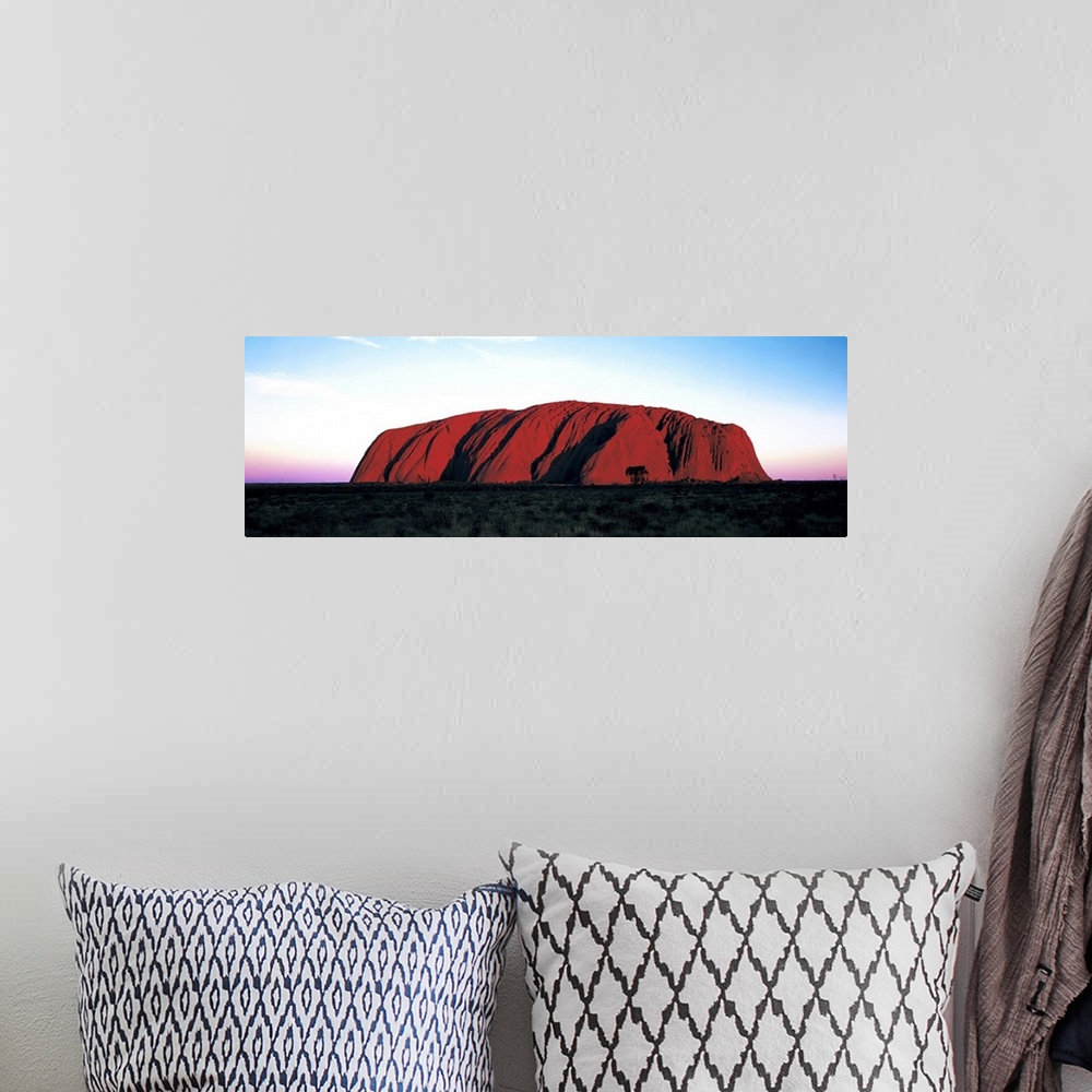 A bohemian room featuring The Ayers Rock is photographed in wide angle view during a sunset which lines the horizon with wa...