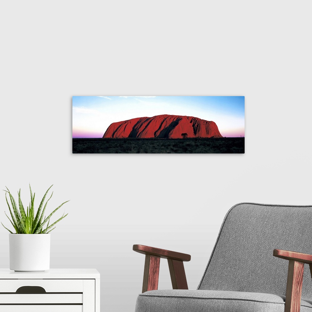 A modern room featuring The Ayers Rock is photographed in wide angle view during a sunset which lines the horizon with wa...
