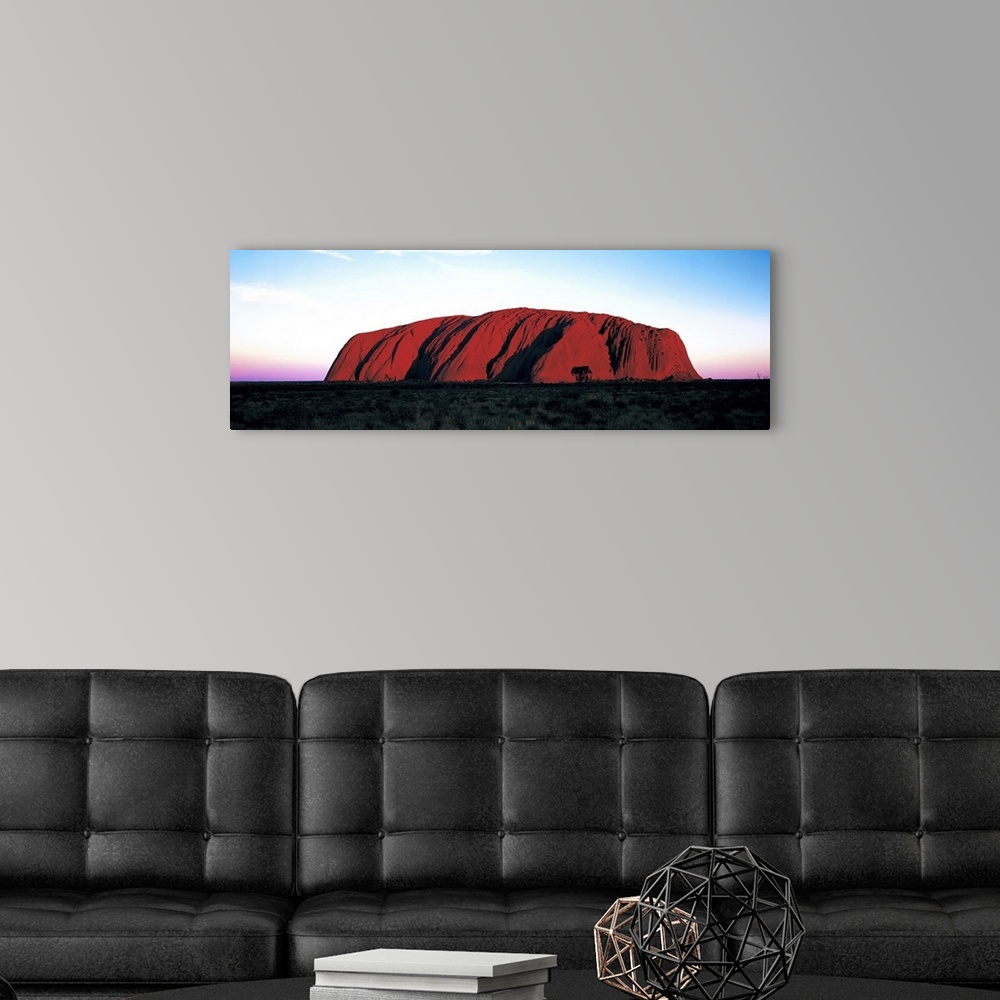 A modern room featuring The Ayers Rock is photographed in wide angle view during a sunset which lines the horizon with wa...