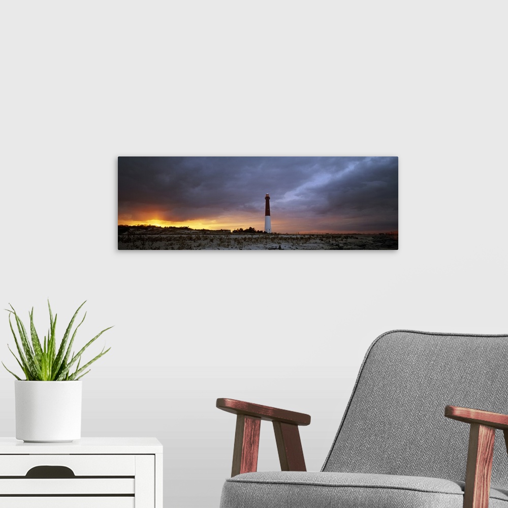 A modern room featuring Panoramic photograph of watchtower on beach at dusk.  The sky is cloudy and the sun is barely vis...