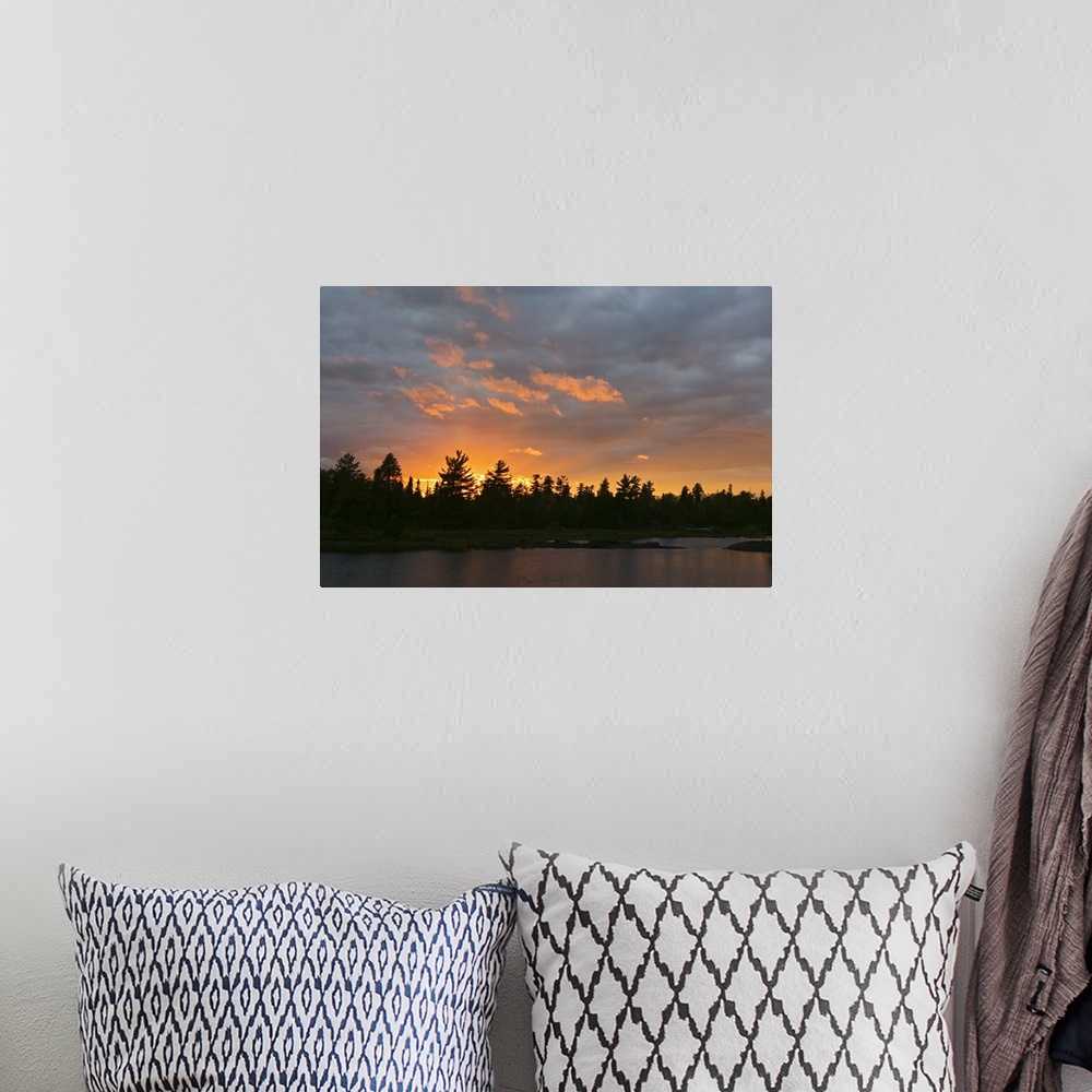 A bohemian room featuring A beautiful picture taken of a thick forest from across a lake with a sun setting behind it silho...