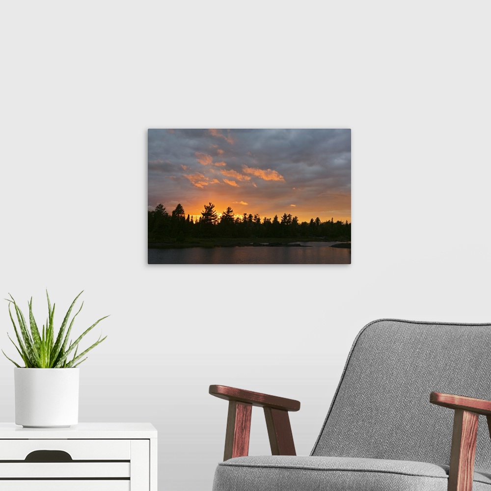 A modern room featuring A beautiful picture taken of a thick forest from across a lake with a sun setting behind it silho...