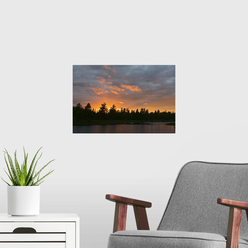 A modern room featuring A beautiful picture taken of a thick forest from across a lake with a sun setting behind it silho...