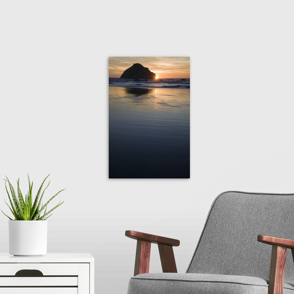 A modern room featuring A setting sun peaks from behind a large rock formation in the ocean water.