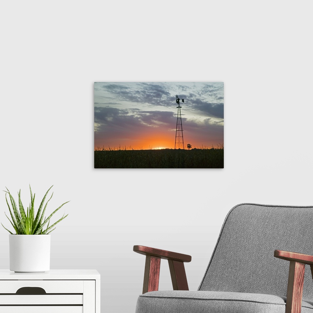 A modern room featuring A tall windmill rises above a crop field on a farm with just the edge of the setting sun peeking ...