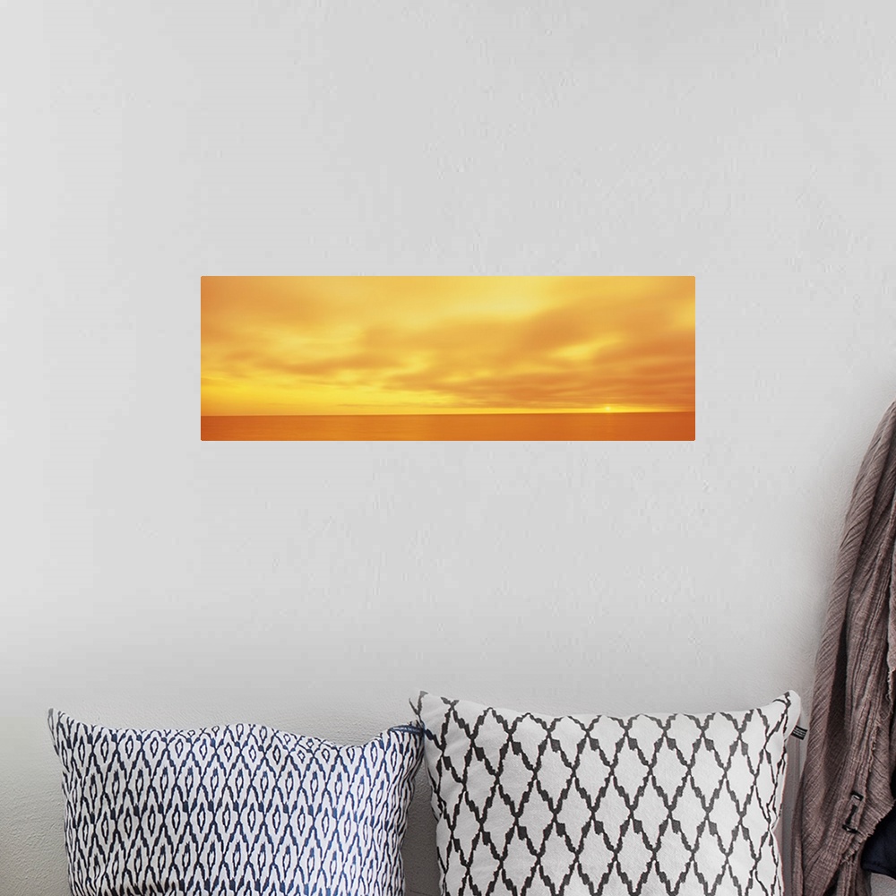 A bohemian room featuring Panoramic photograph of calm wave less ocean under a cloudy sky.